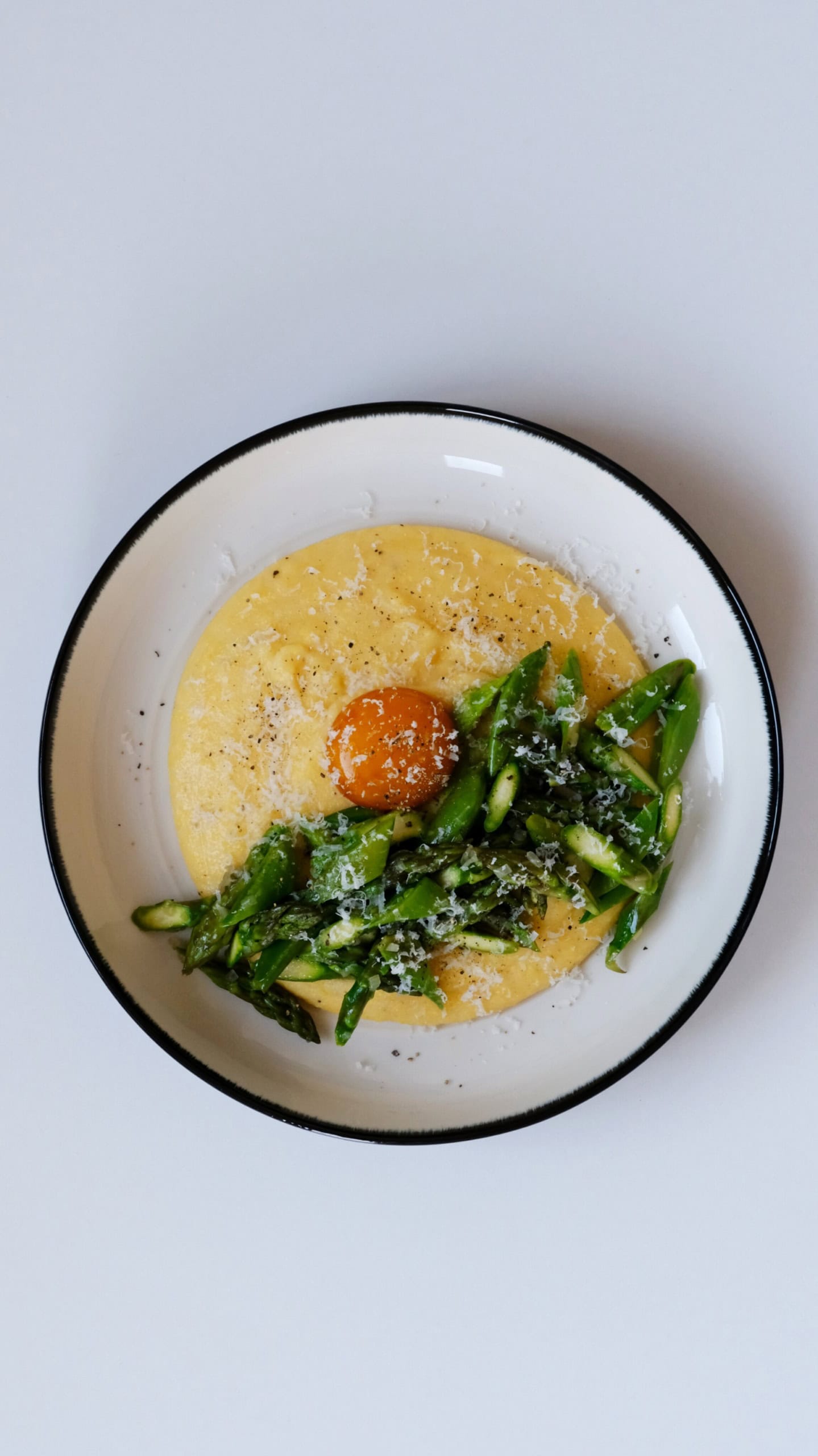 In einem tiefen Teller ist eine Portion Polenta mit gehacktem, grünen Spargel angerichtet. Genau in der Mitte ist ein pochiertes Eigelb platziert, über alles wurde Käse gerieben.