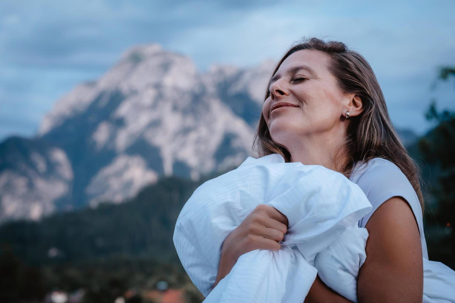 Frau hält zufrieden eine Bettdecke im Arm, im Hintergrund die Berge bei Füssen im Allgäu