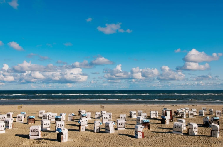 Auf der Ostfriesischen Insel Spiekeroog stehen zahlreiche Strandkörbe am Strand, bereit für den Urlaub.