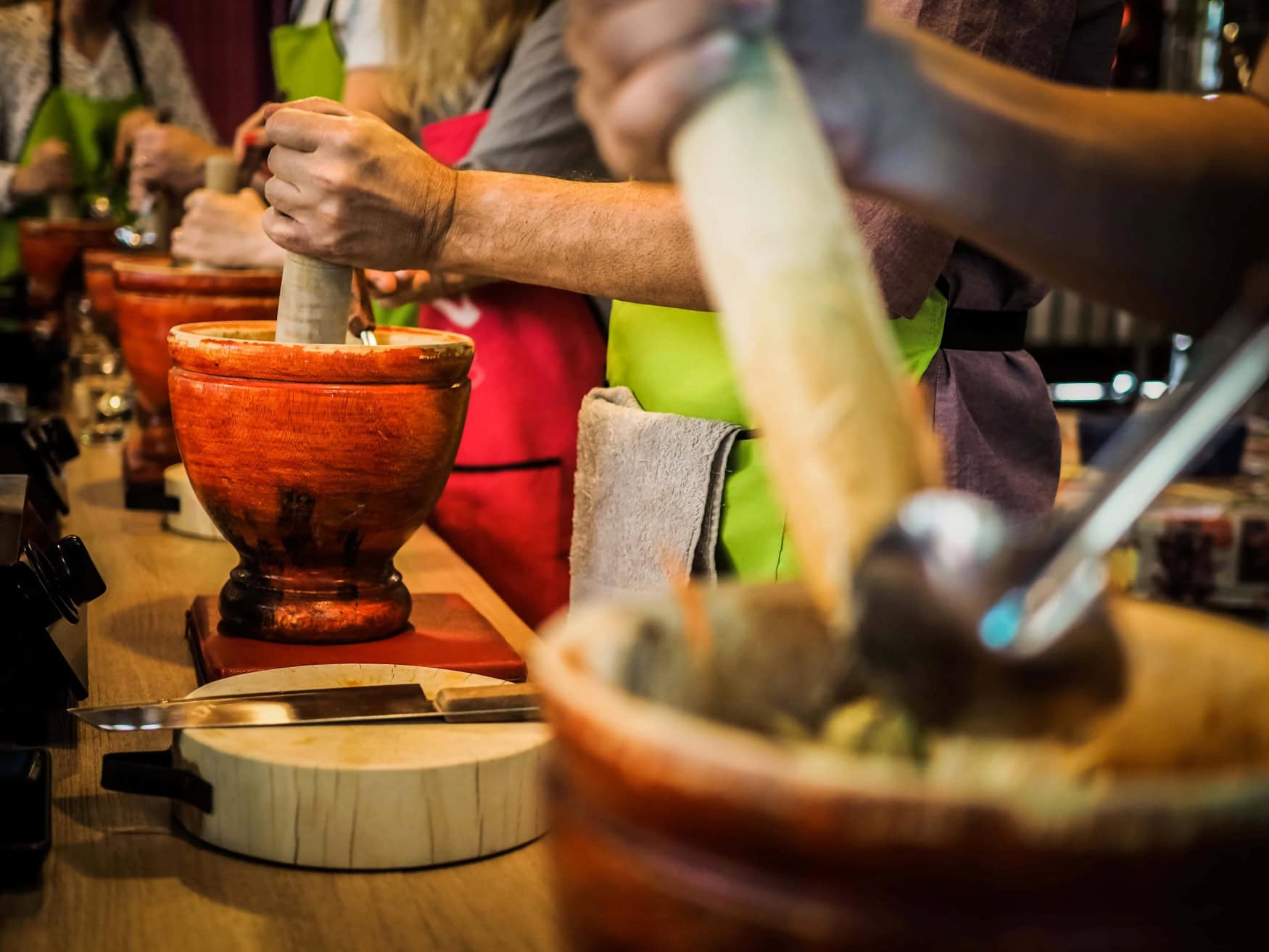 Nahaufnahme von Teilnehmern einer thailändischen Cookingclass, zu sehen sind die Hände mehrerer Personen, die mit einem Mörser arbeiten.