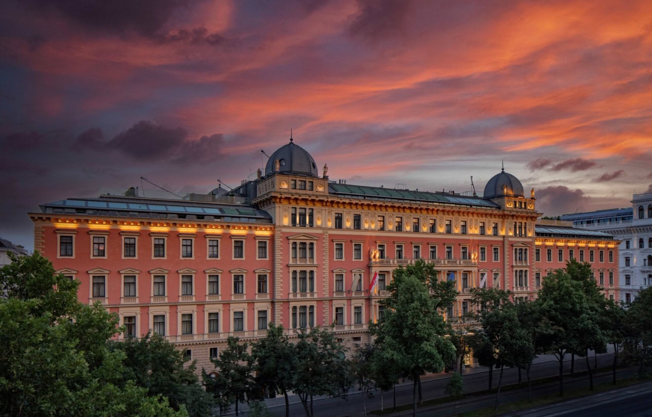 Das Anantara Palais Hansen Vienna Hotel von außen; ein klassizistischer Palas mit lachsroter Fassade, darüber der rote Abendhimmel.