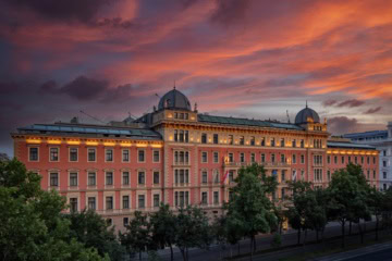 Das Anantara Palais Hansen Vienna Hotel von außen; ein klassizistischer Palas mit lachsroter Fassade, darüber der rote Abendhimmel.