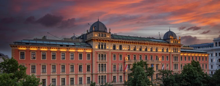Das Anantara Palais Hansen Vienna Hotel von außen; ein klassizistischer Palas mit lachsroter Fassade, darüber der rote Abendhimmel.