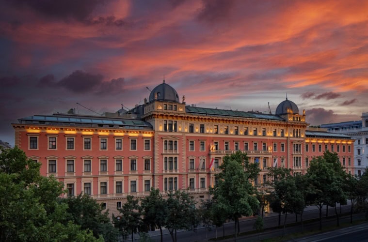 Das Anantara Palais Hansen Vienna Hotel von außen; ein klassizistischer Palas mit lachsroter Fassade, darüber der rote Abendhimmel.