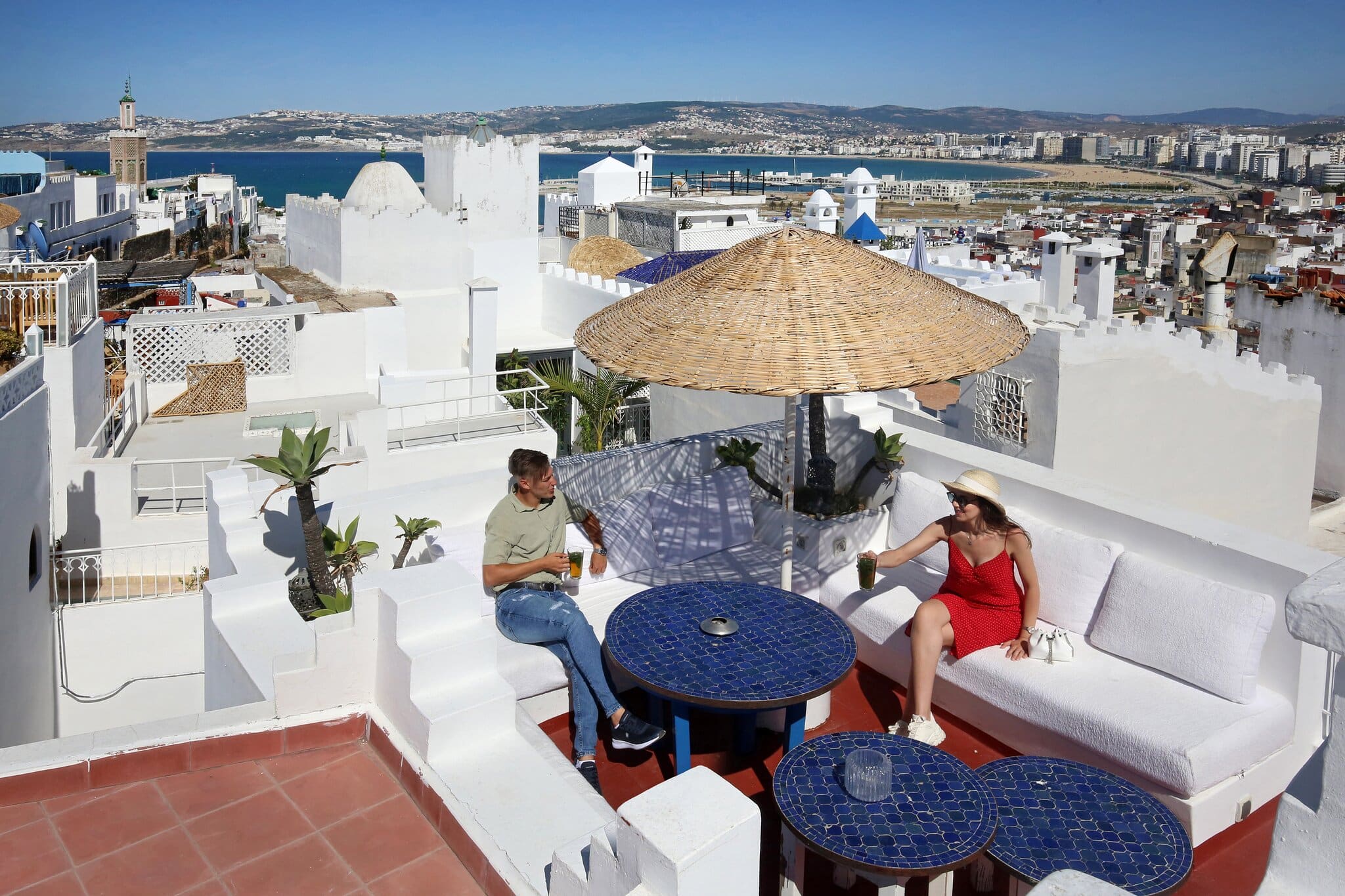 Paar auf einer Dachterrasse mit Mosaiktischen und Blick ueber die weisse Medina und die Bucht von Tanger.