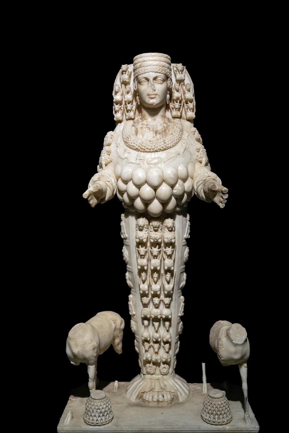 Marmorstatue der Artemis von Ephesus mit reich verziertem Schmuck und Tierreliefs vor schwarzem Hintergrund.