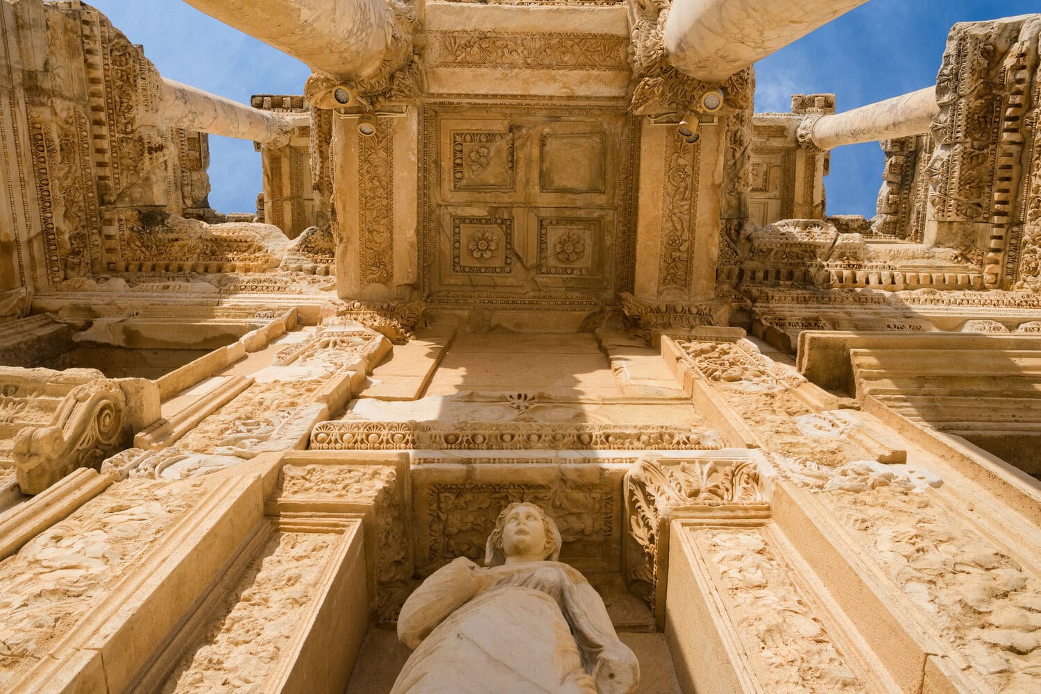Reich verzierte Kassettendecke der Celsus-Bibliothek mit einer Statue, von unten fotografiert.