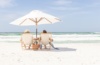 Händchenhaltendes Pärchen unter einem Sonnenschirm auf Liegestühlen am Strand von Florida