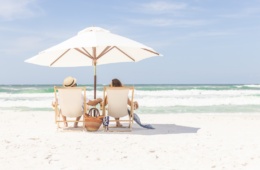 Händchenhaltendes Pärchen unter einem Sonnenschirm auf Liegestühlen am Strand von Florida
