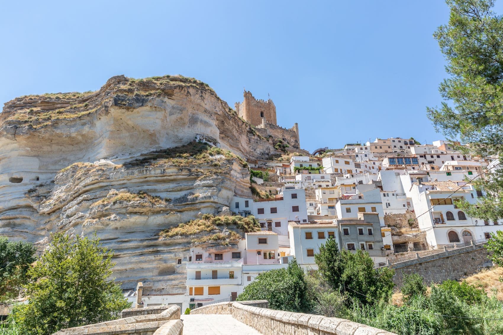 Die historische Steinbrücke von Alcalá del Júcar führt zu den weißen Häusern und der Burg über den markanten Felsen in Kastilien-La Mancha, Spanien.