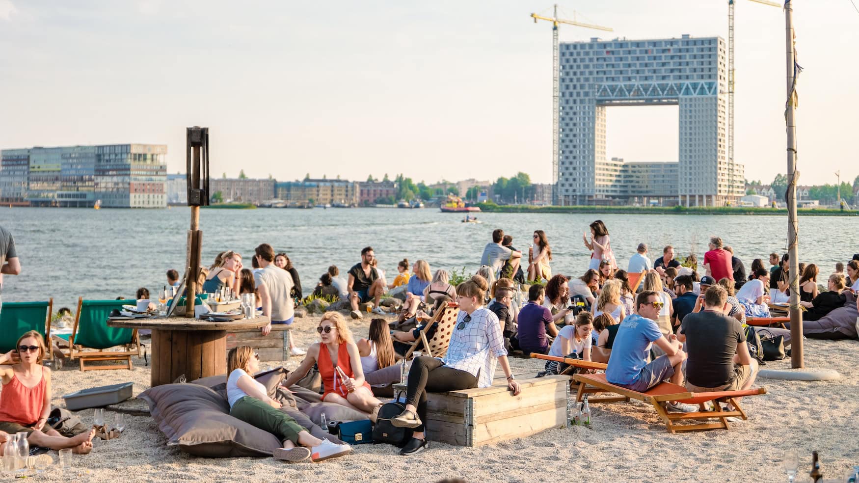 Menschen am sandigen Ufer mit Blick auf das Pontsteiger-Gebäude in Amsterdam Noord