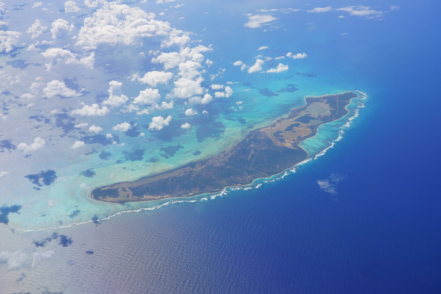  Luftaufnahme aus großer Höhe zeigt Anegada als flachen, länglichen Streifen Land, umgeben vom türkisfarbenen Korallenriff und dem tiefblauen Atlantik