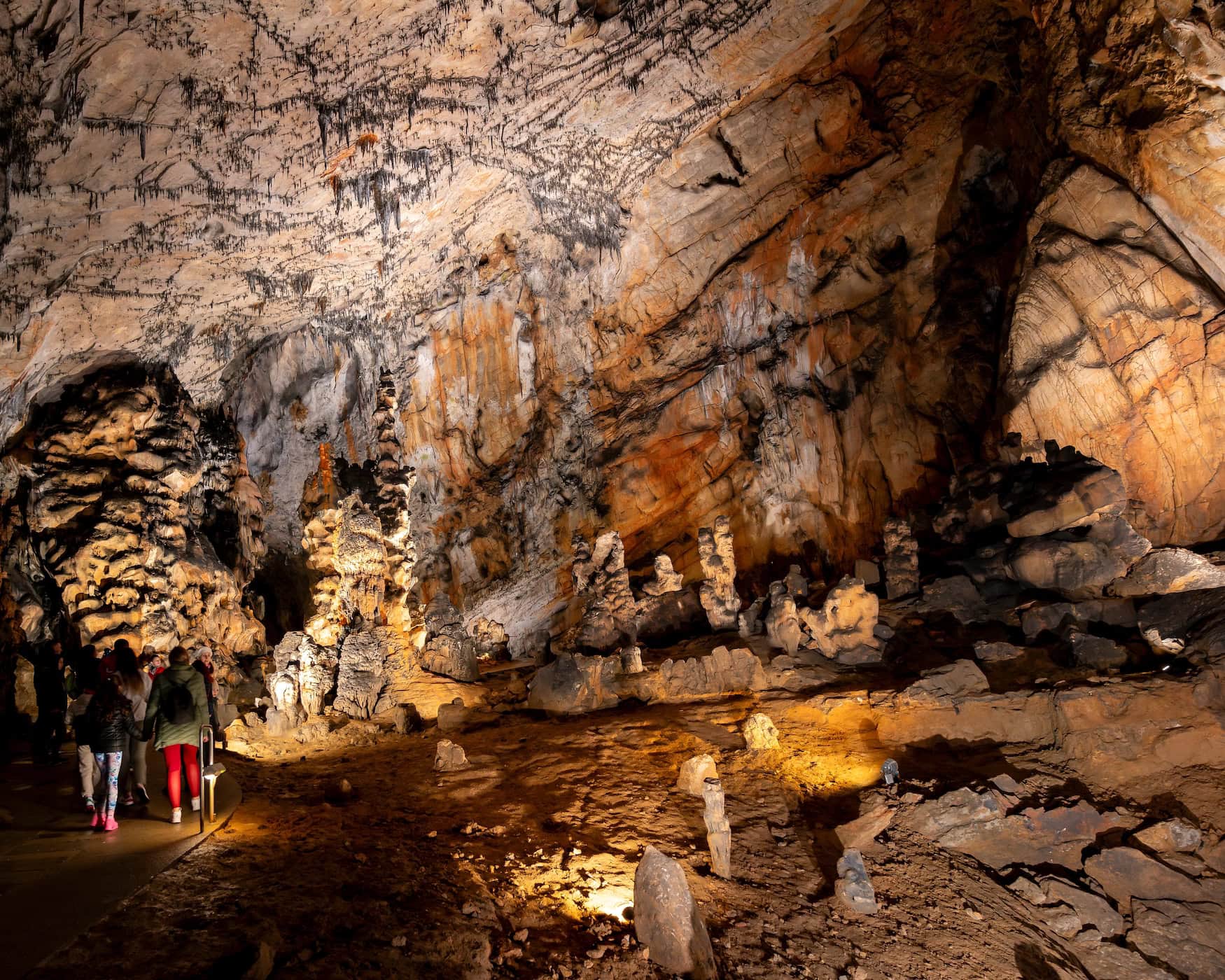 Besucher stehen in einer weitläufigen Halle der Baradla-Höhle im Aggteleker Karst, Ungarn – beleuchtete Stalagmiten und Tropfsteinformationen an Wänden und Decke