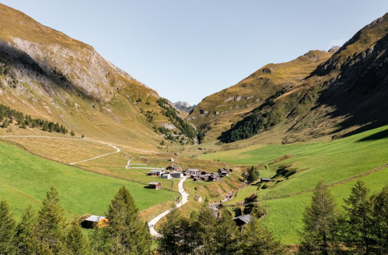 Die Fane Alm in Gitschberg Jochtal in Südtirol. Ein paar Häuser stehen in einem Tal neben einem kleinen Bach inmitten von Wiesen bedeckten Bergen.