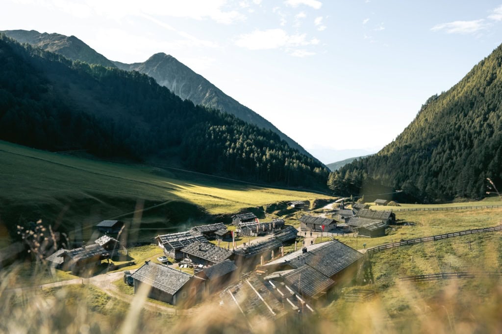 Häuser stehen auf der Fane Alm im Valstal. Drumherum sind Berge, die mit Tannen bewachsen sind