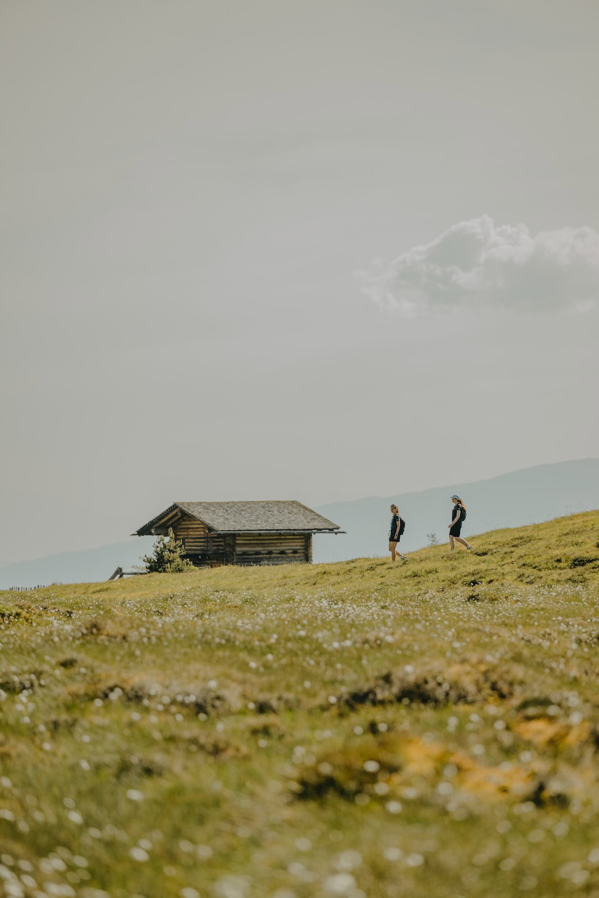 Zwei Personen wandern bergab an einer Hütte vorbei auf der Rodenecker-Lüsner-Alm in Gitschberg Jochtal