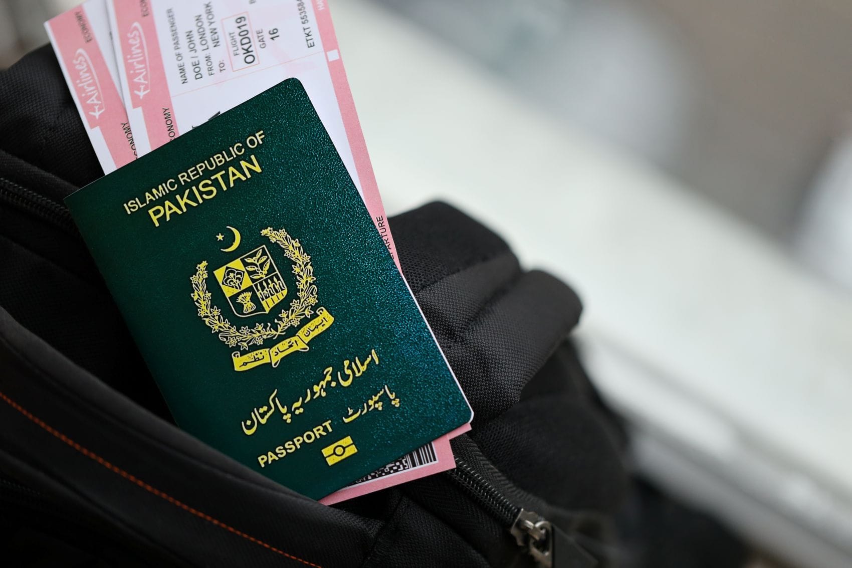 Grüner Reisepass aus Pakistan mit Bordkarte auf einem Rucksack am Flughafen.
