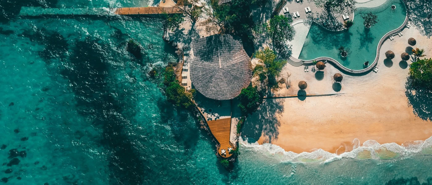 Luftaufnahme des Poolbereichs eines Luxusresorts bei Sansibar; das Meer rund um den Strandabschnitt ist türkisblau und klar.