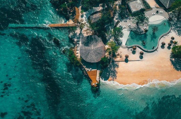 Luftaufnahme des Poolbereichs eines Luxusresorts bei Sansibar; das Meer rund um den Strandabschnitt ist türkisblau und klar.