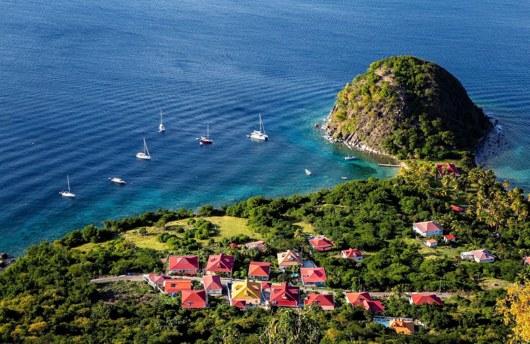 Luftbild der Îles des Saintes mit dem Pain-de-Sucre-Felsen, roten Ziegeldächern und Yachten im türkisblauen Wasser der Karibik