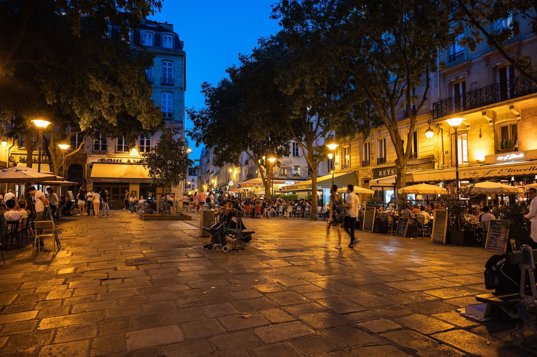 Belebter Platz mit beleuchteten Cafés und Terrassen am Sommerabend im Pariser Viertel Le Marais