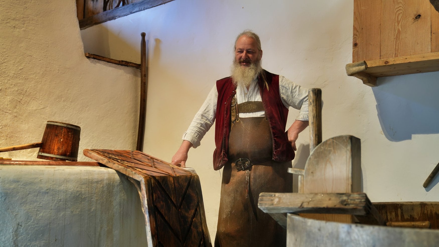 Brauer in historischer Tracht mit weißem Hemd, roter Weste und Lederschürze steht an alten Holzsudgefäßen in der historischen Brauerei des Markus Wasmeier Freilichtmuseums.