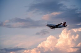 Analysierte Flugzeugbild und formulierte präzisen Alt-Text»Verkehrsflugzeug im Landeanflug mit ausgefahrenem Fahrwerk vor rosa beleuchteten Wolken im Abendhimmel.