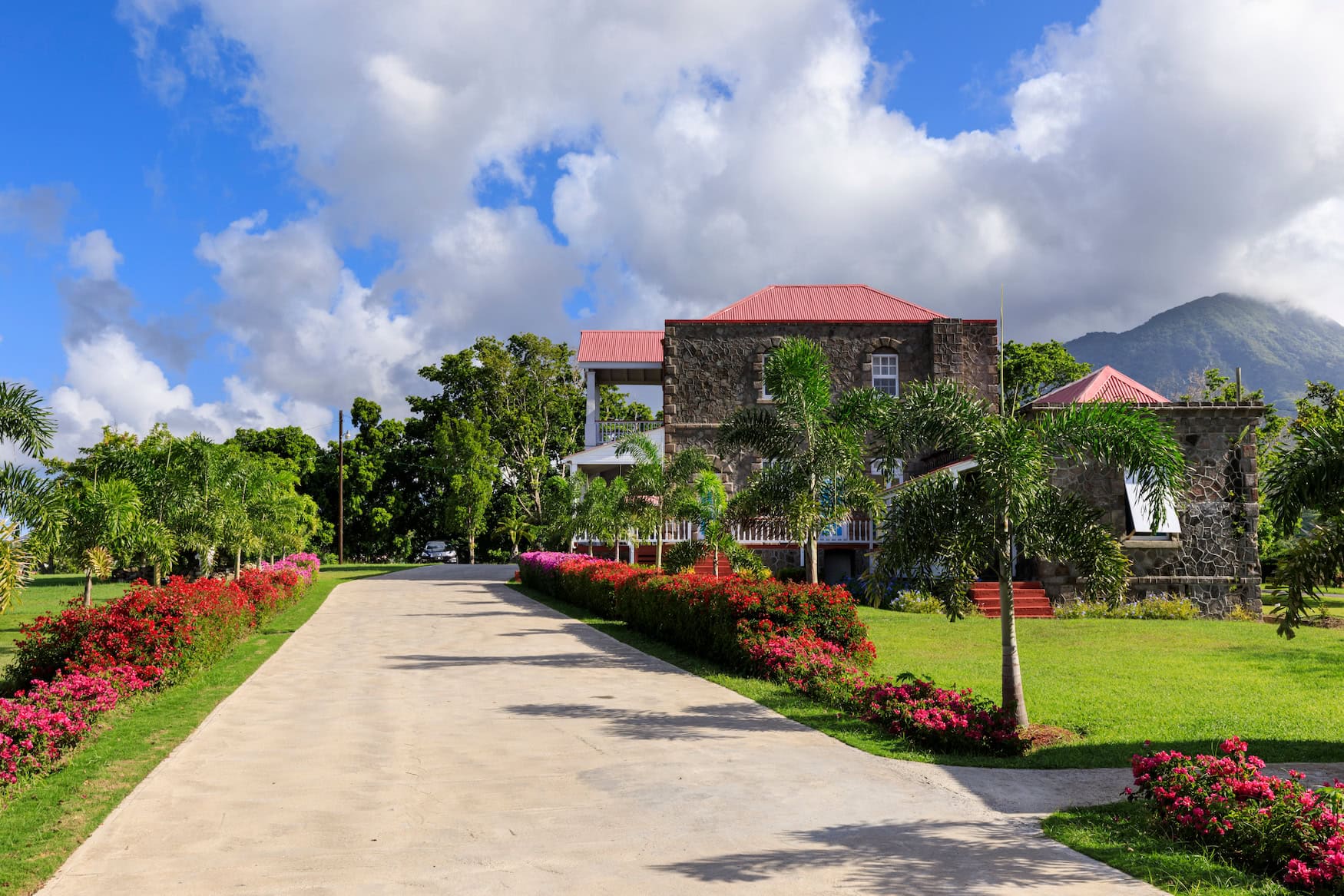 Historisches Steingebäude eines ehemaligen Plantagenhotels auf Nevis mit rotem Dach, gesäumt von Blumen, mit dem Nevis Peak im Hintergrund