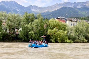 Teilnehmer einer geführten Rafting-Tour auf dem Inn vor der Kulisse der Innsbrucker Altstadt und der Nordkette in Tirol.