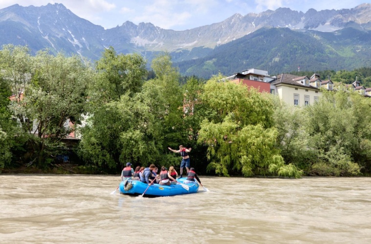 Teilnehmer einer geführten Rafting-Tour auf dem Inn vor der Kulisse der Innsbrucker Altstadt und der Nordkette in Tirol.