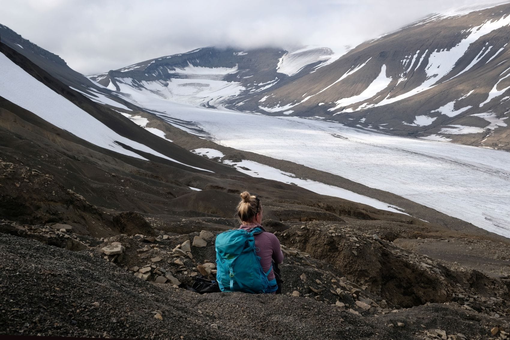 Wanderin blickt auf einen Gletscher in der kargen Berglandschaft Spitzbergens.