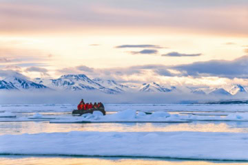 Touristen fahren mit einem Schlauchboot zwischen Eisschollen vor der Bergkulisse Spitzbergens.