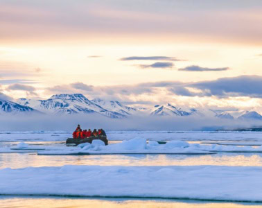 Touristen fahren mit einem Schlauchboot zwischen Eisschollen vor der Bergkulisse Spitzbergens.