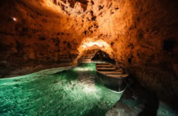 Ein kleines Boot liegt im türkisgrünen Wasser der Tapolca-Seehöhle, Ungarn – warm beleuchtete Felswände und ein Felstor im Hintergrund