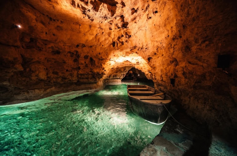 Ein kleines Boot liegt im türkisgrünen Wasser der Tapolca-Seehöhle, Ungarn – warm beleuchtete Felswände und ein Felstor im Hintergrund