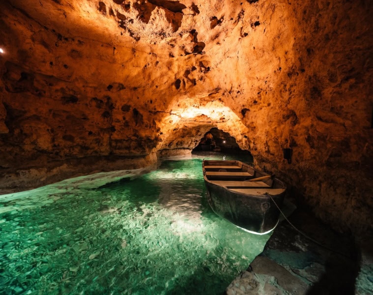Ein kleines Boot liegt im türkisgrünen Wasser der Tapolca-Seehöhle, Ungarn – warm beleuchtete Felswände und ein Felstor im Hintergrund