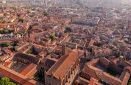 Drohnenaufnahme der Altstadt von Toulouse mit charakteristischen rosa-roten Backsteingebäuden und der Place du Capitole.