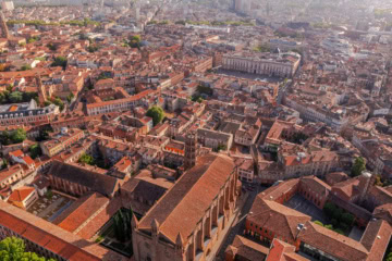 Drohnenaufnahme der Altstadt von Toulouse mit charakteristischen rosa-roten Backsteingebäuden und der Place du Capitole.
