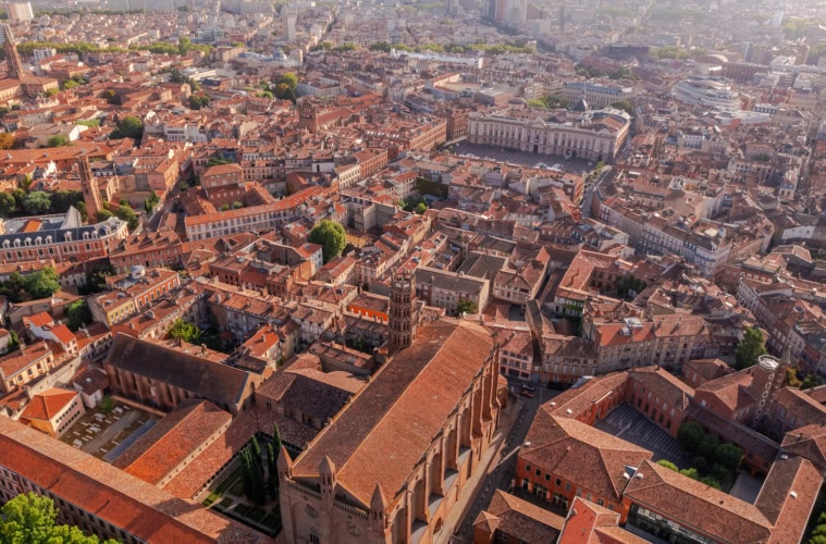 Drohnenaufnahme der Altstadt von Toulouse mit charakteristischen rosa-roten Backsteingebäuden und der Place du Capitole.