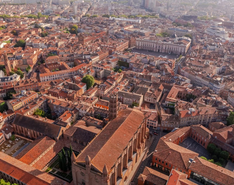 Drohnenaufnahme der Altstadt von Toulouse mit charakteristischen rosa-roten Backsteingebäuden und der Place du Capitole.