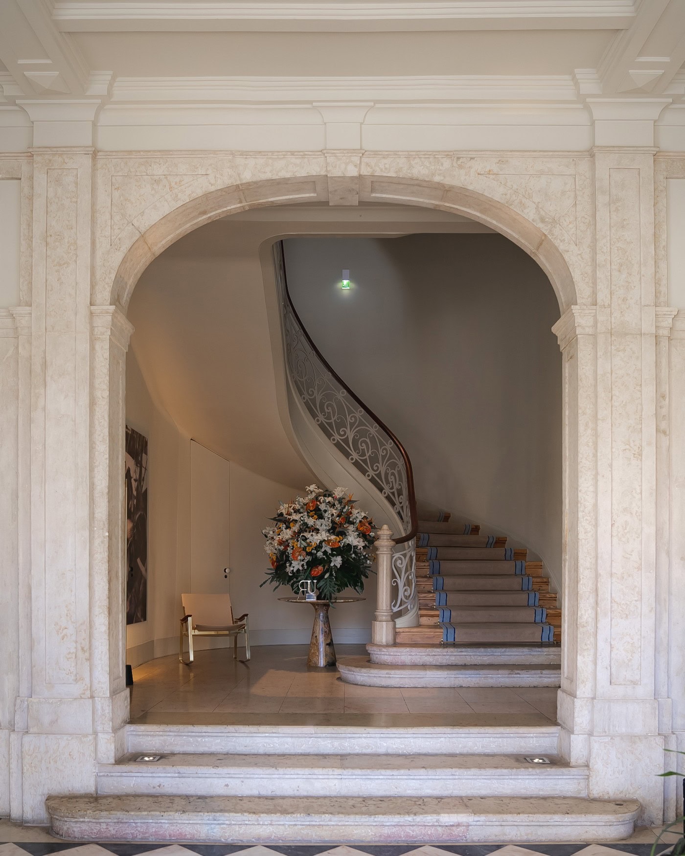 Hinter einem steinernen Durchgang in einem historischen Palas führt eine kunstvolle, hölzerne Wendeltreppe nach oben.