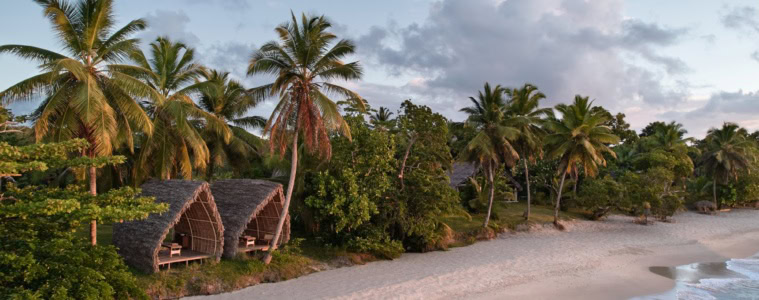 Luftaufnahme des Strands am Voaara auf Madagaskar im Abendlicht: zwei Spa-Pavillons mit gewölbten Strohdächern am Waldrand, davor ein langer weißer Sandstrand mit sanften Wellen.