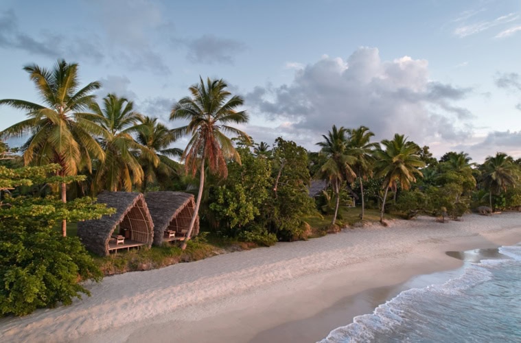 Luftaufnahme des Strands am Voaara auf Madagaskar im Abendlicht: zwei Spa-Pavillons mit gewölbten Strohdächern am Waldrand, davor ein langer weißer Sandstrand mit sanften Wellen.
