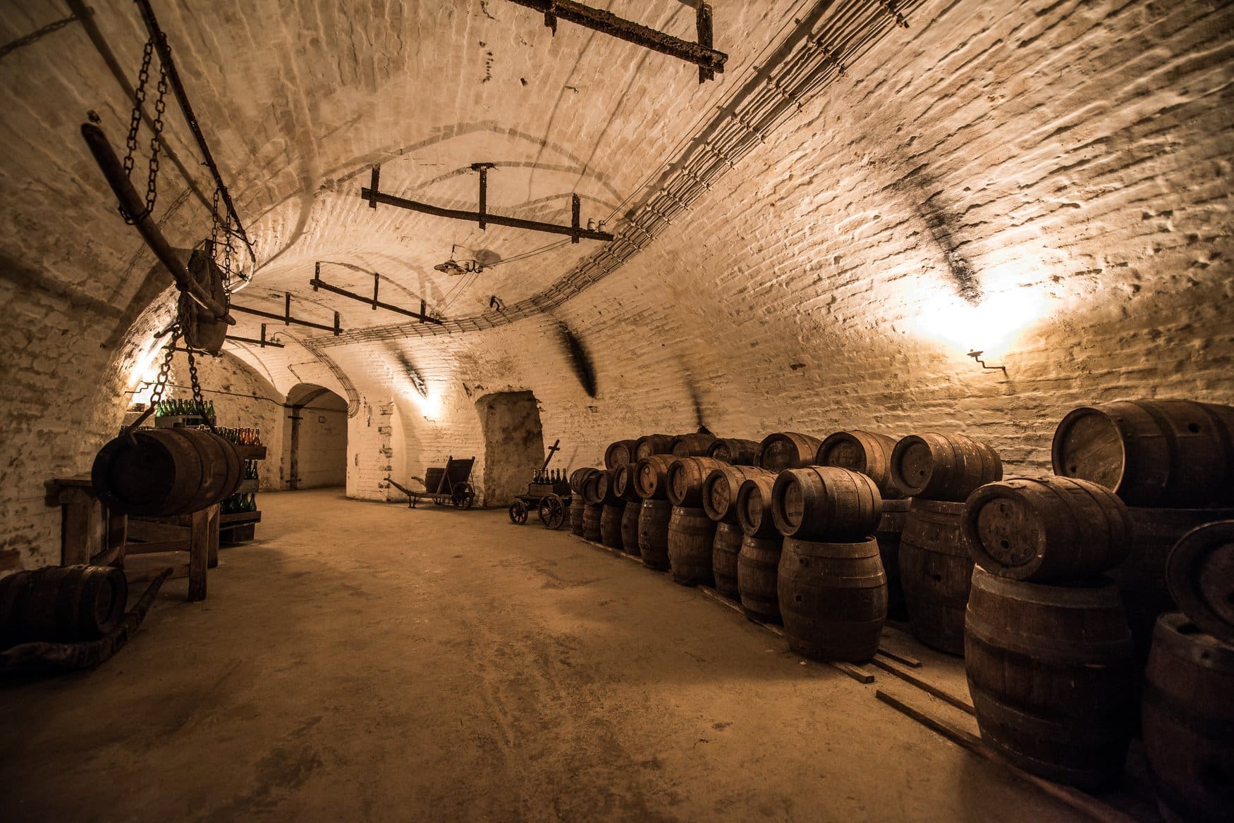 Historische Bierkatakomben unter Wasserburg am Inn mit gewölbten Ziegelsteindecken, aufgereihten Holzfässern und warmem Licht, das den langen Kellergang beleuchtet.