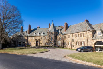 Außenansicht des Hotels The Graylyn Estate, ein historistisches Schloss aus grauem Bruchstein, davor eine Auffahrt.