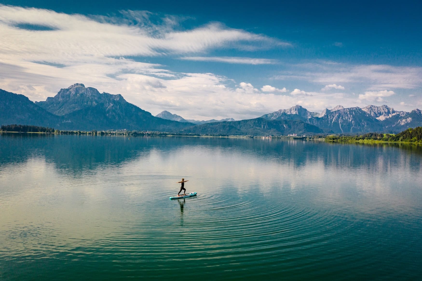Eine Frau macht Yoga auf einem SUP auf dem Forggensee.