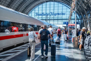 eisende mit Koffern gehen am Frankfurter Hauptbahnhof an einem ICE der Deutschen Bahn entlang.
