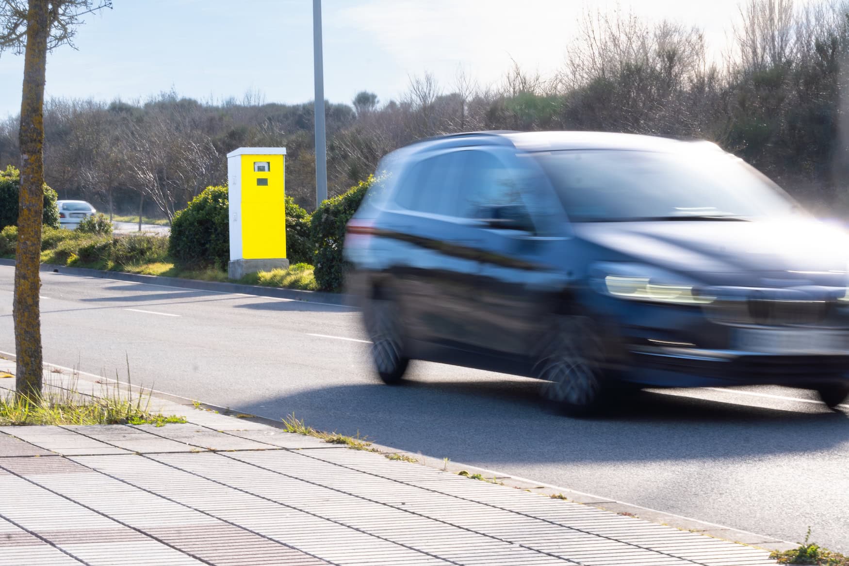 Blitzer am Straßenrand, während ein Auto unscharf vorbeifährt