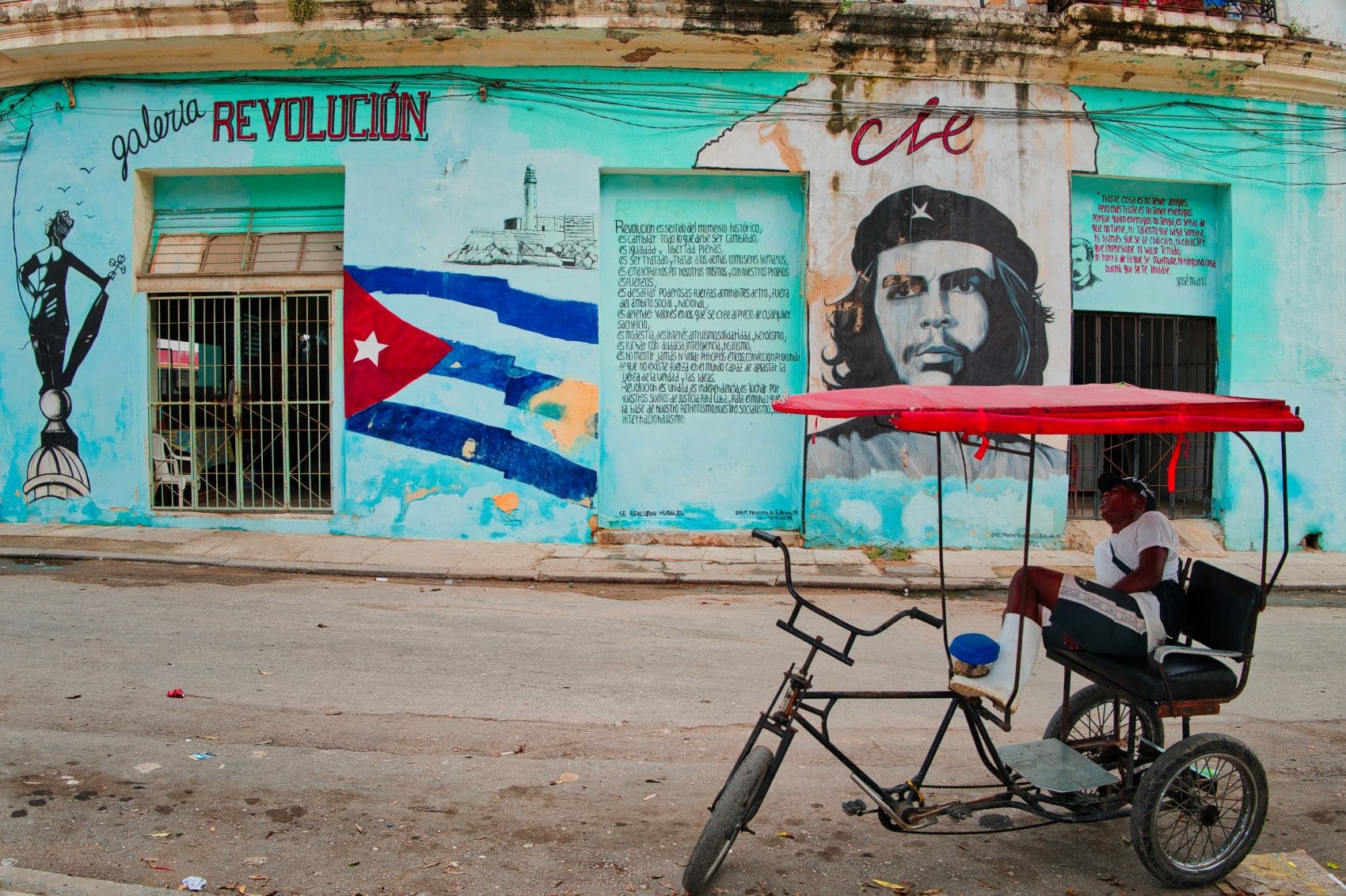 ahrradtaxi vor einem Wandgemälde mit Che Guevara und Revolutionsparolen in Havanna auf Kuba.
