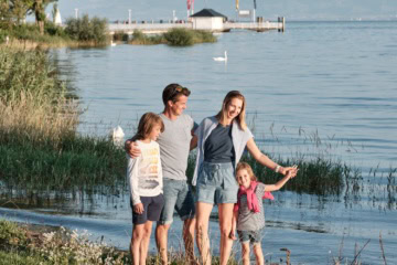 Ein Mann, eine Frau und zwei Kinder stehen am Ufer des Bodensees im Sommer.